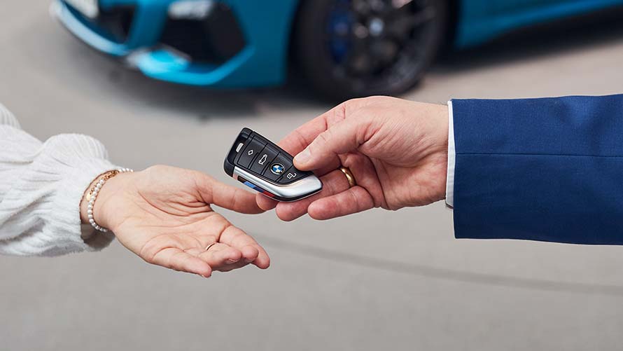 Schluesseluebergabe vor einem metallisch blauen BMW Modell in der BMW Welt