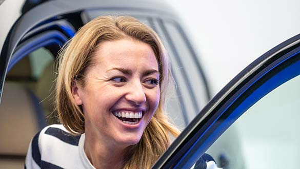 PREMIUM Fahrzeugabholung Frau steigt lächelnd in ihren neuen BMW bei der Auto Abholung in der BMW Welt