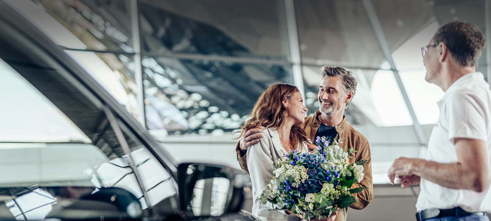 Auto Abholung BMW Welt Glückliches Paar bei der Fahrzeugübergabe in der BMW Welt mit Berater und Blumenstrauss
