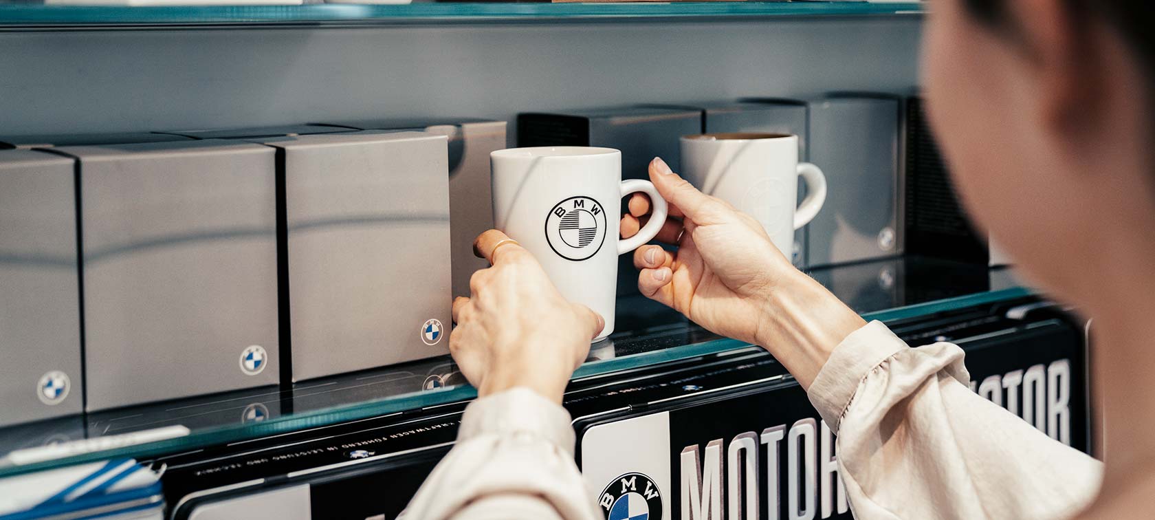 mitarbeiterin stellt tasse in regal im bmw welt shop