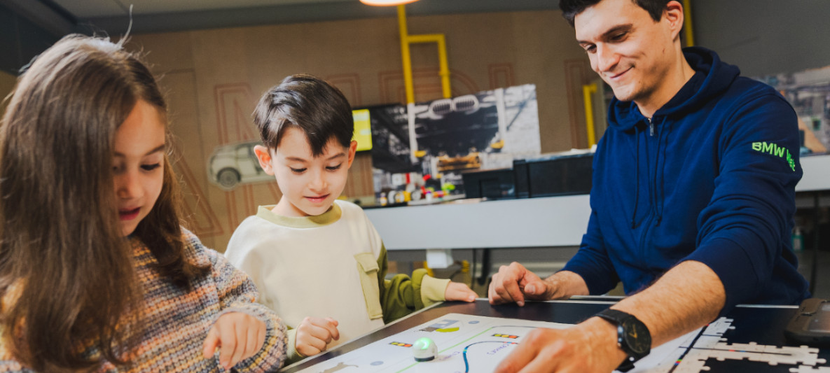 BMW Welt Workshop BMW Welt Workshopleiter erklärt zwei Kindern die Funktionsweise von Schaltkreisen anhand eines kindgerechten Modells