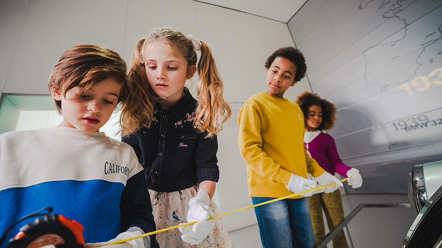 BMW Klassen- und Gruppenausflüge Detektivworkshop Kinder vermessen Fahrzeuge im BMW Museum, um Hinweise zu finden