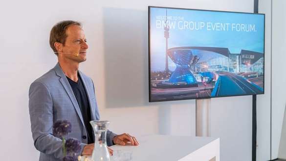 Bühnentechnik Mann in grauem Sakko und Mikrofon steht neben Präsentationsbildschirm im BMW Welt Business Center